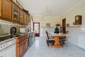 Une cuisine avec des meubles de rangement en bois, une cuisinière blanche, une table à manger avec des chaises et un lustre.