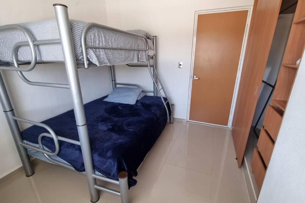 A bunk bed with a metal frame and a blue bedspread in a room with a wooden door and a tiled floor.