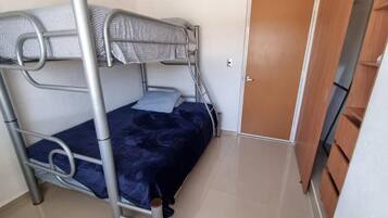 A bunk bed with a metal frame and a blue bedspread in a room with a wooden door and a tiled floor.