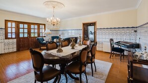 Ein Esszimmer mit einer Chandelieber, einem Holzessttisch, Stühlen und einem Klavier.