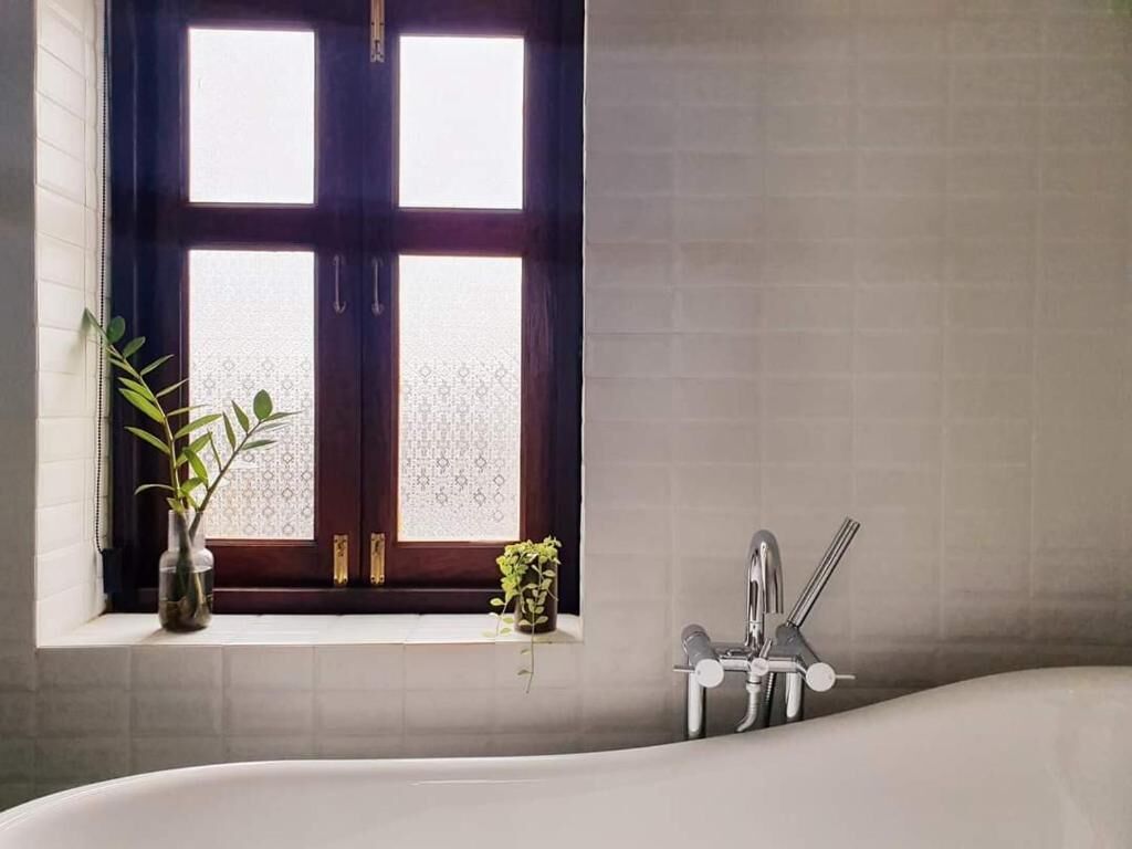 Un baño con bañera, una ventana de vidrio esmerilado y una planta en el alféizar.