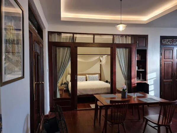 Una habitación de hotel con una cama, una mesa de comedor con sillas, una mesita con un florero y una estantería.