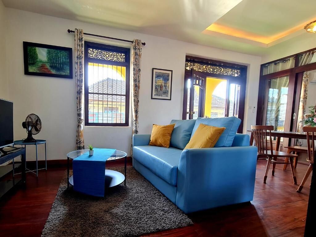 A living room with a blue sofa, a small round table, a TV, and a fan.