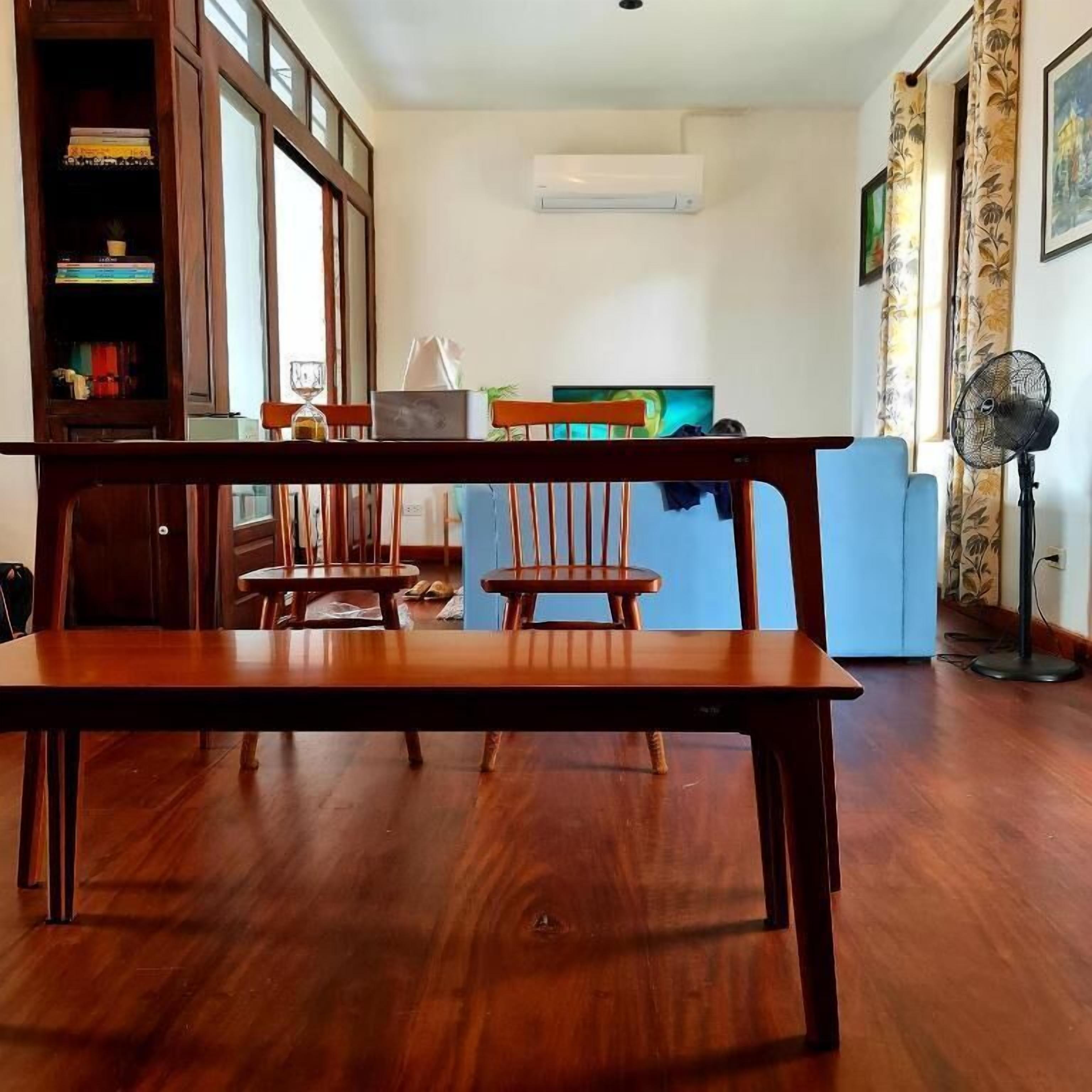 A dining area with a wooden table and chairs, a bookshelf, and a television in the background.