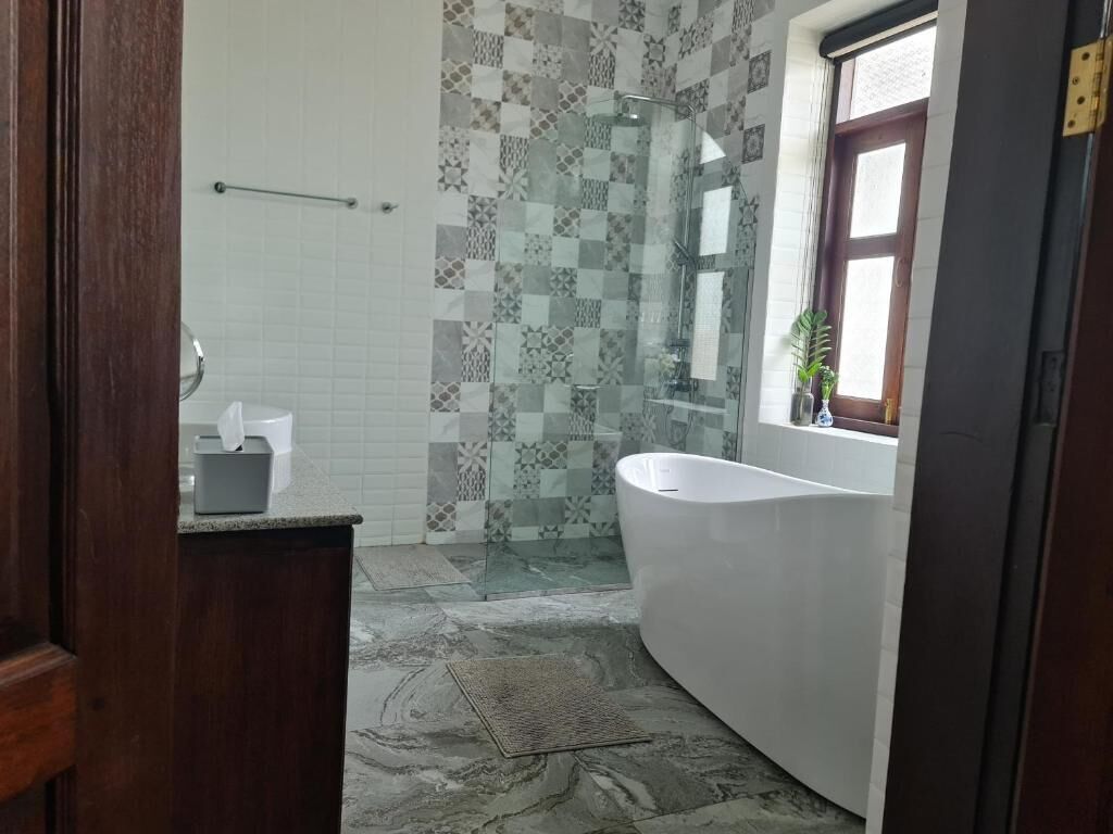 A bathroom with a glass shower, a white bathtub, and a window with a plant.