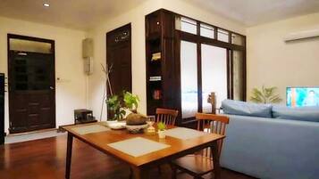 A dining area with a wooden table and chairs, a potted plant, and a blue sofa in the background.