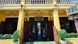 Un edificio amarillo con un balcón, un letrero que dice "Indonesian" y macetas con plantas en la entrada.