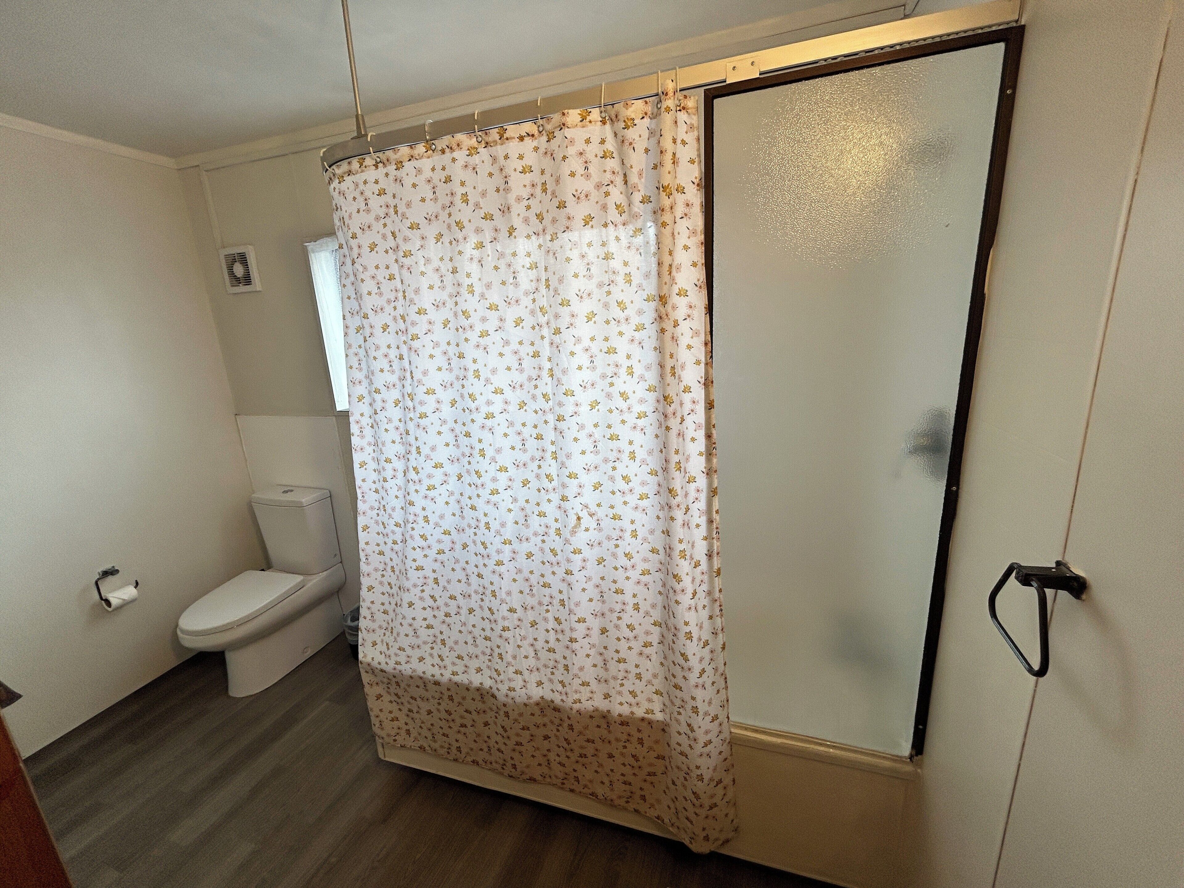 A bathroom with a toilet, a shower curtain, and a glass door.