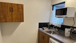 A compact kitchen with wooden cabinets, a stainless steel sink, a microwave, and a dishwasher. - Aquarious motor inn (Hamilton)