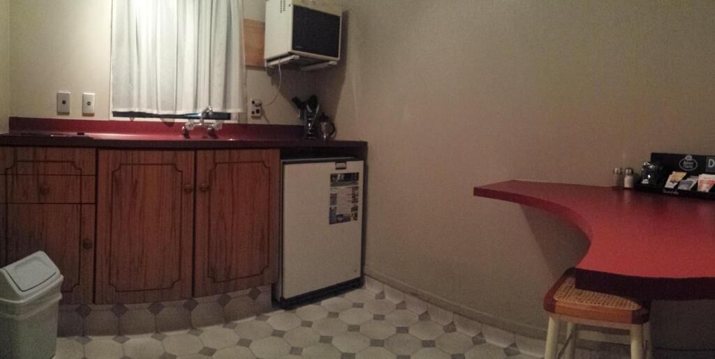 A compact kitchen with wooden cabinets, a small refrigerator, a microwave, and a red countertop.