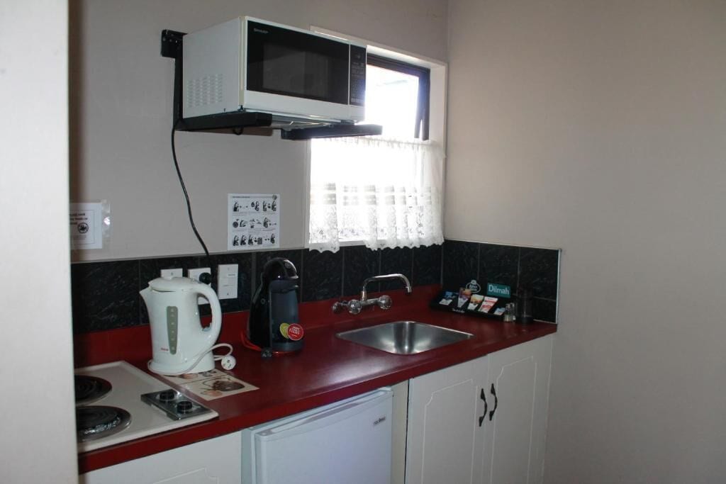 Cozinha compacta equipada com micro-ondas, chaleira, máquina de café e pia.