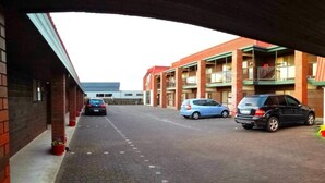 A parking area with cars parked under a building with brick walls and a flat roof. - Aquarious motor inn (Hamilton)