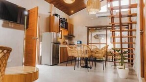 A modern kitchen with wooden cabinets, a refrigerator, and a dining area with wicker chairs and a table. - Villa Adara by Araw Residences (Alfonso)
