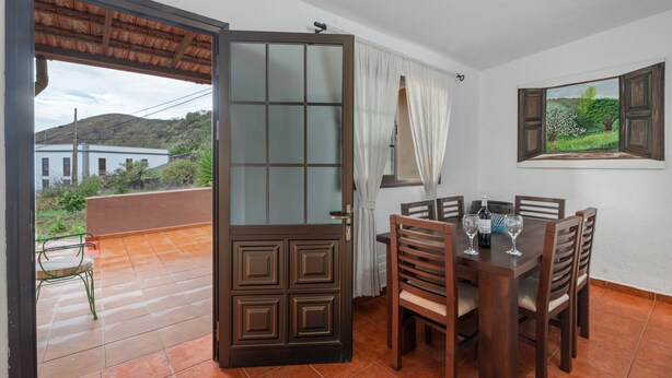 A dining area with a table and chairs, a view of the outdoors, and a door leading to a balcony. - Holiday Home 'Mary Valverde' with Sea View, Private Terrace and Wi-Fi (Villa de Valverde)