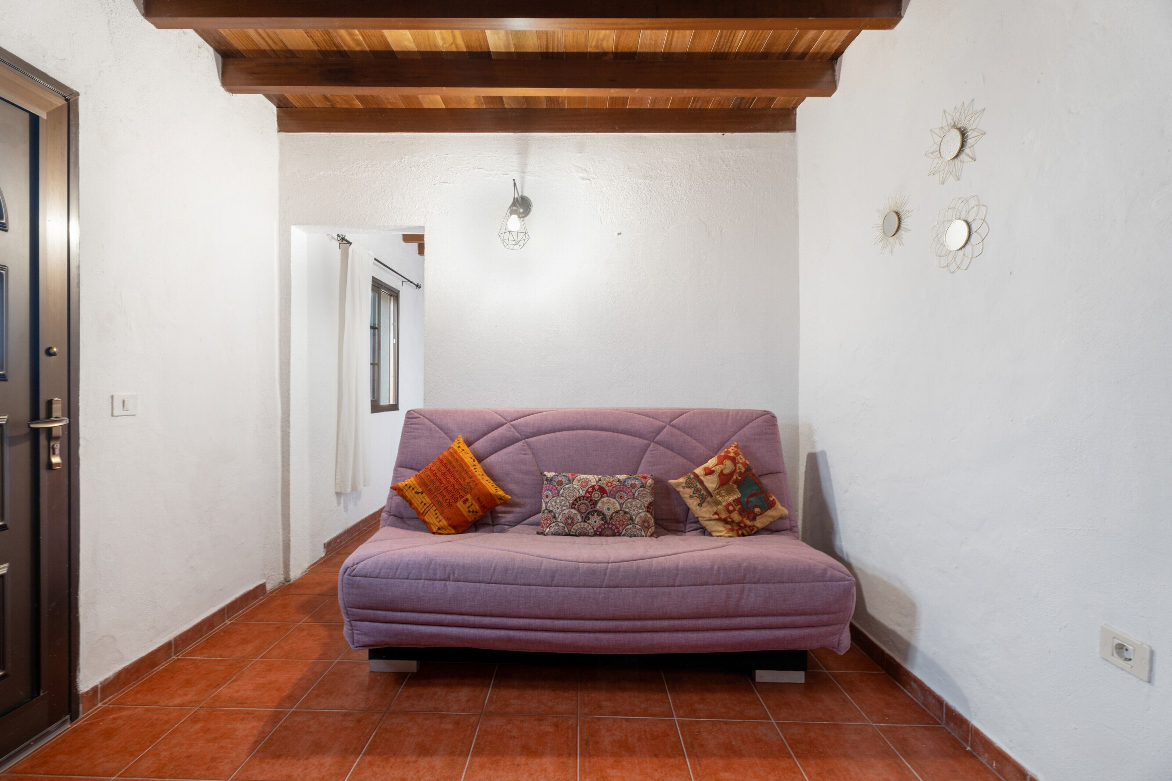 A room with a purple sofa, a wooden ceiling, and a white wall with decorative mirrors.