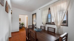 A dining area with a wooden table, chairs, a blue glass bowl, and a window with curtains. - Holiday Home 'Mary Valverde' with Sea View, Private Terrace and Wi-Fi (Villa de Valverde)