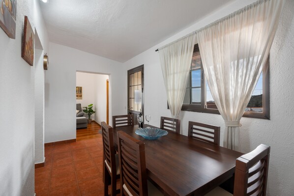 A dining area with a wooden table, chairs, a blue glass bowl, and a window with curtains.