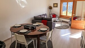 Zona pranzo con tavolo rotondo, sedie e vassoio nero. Sullo sfondo, un divano grigio e un cuscino rosso.