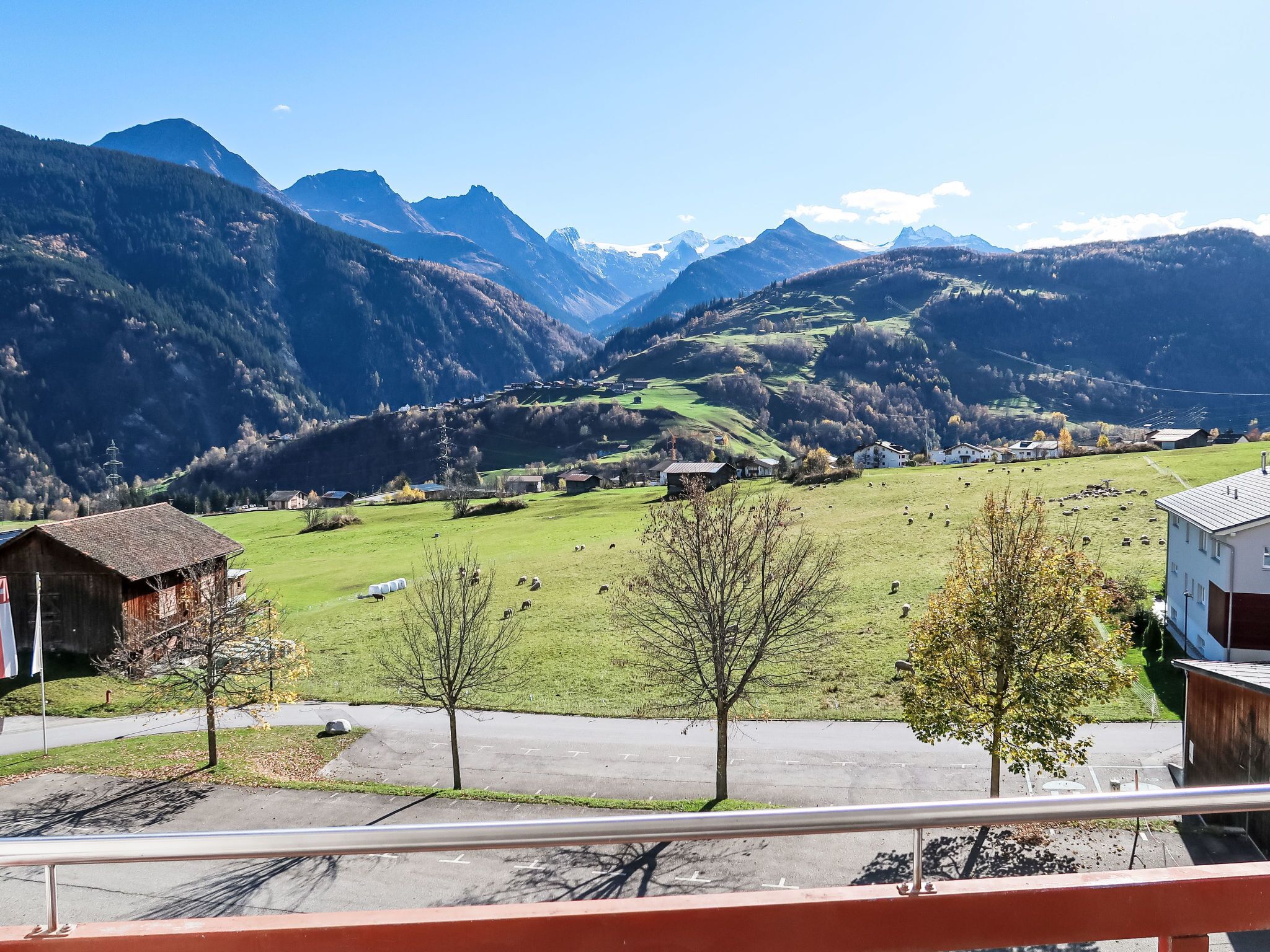 A mountain landscape with a village, including a road, a few buildings, and grazing sheep.