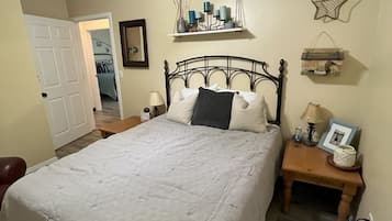 A bedroom with a bed, a nightstand, a ceiling fan, a wall shelf with decorative items, and a door leading to another room.