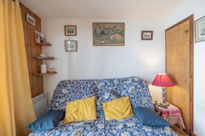 Une pièce avec un canapé à motifs, deux coussins jaunes, une lampe rouge et des tableaux encadrés accrochés au mur.