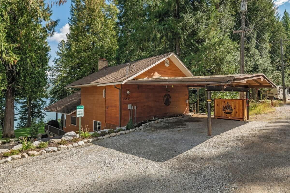 Un chalet rustique doté d’un porche abrité, entouré d’arbres et bordé d’une allée en gravier.