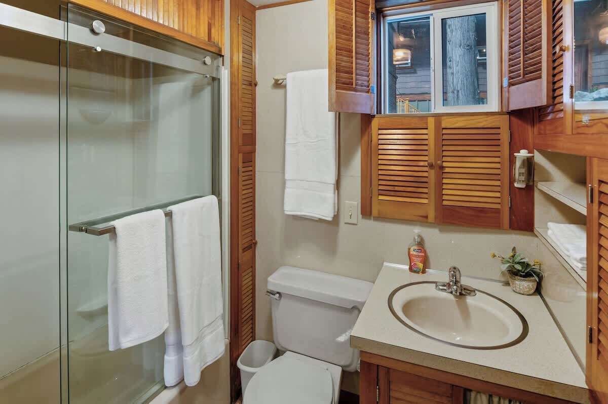 A bathroom with a glass shower enclosure, a toilet, a sink with a mirror, and wooden cabinets.