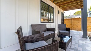 Ein überdachter Patio-Bereich mit Korbmöbeln und einem Glastisch.
