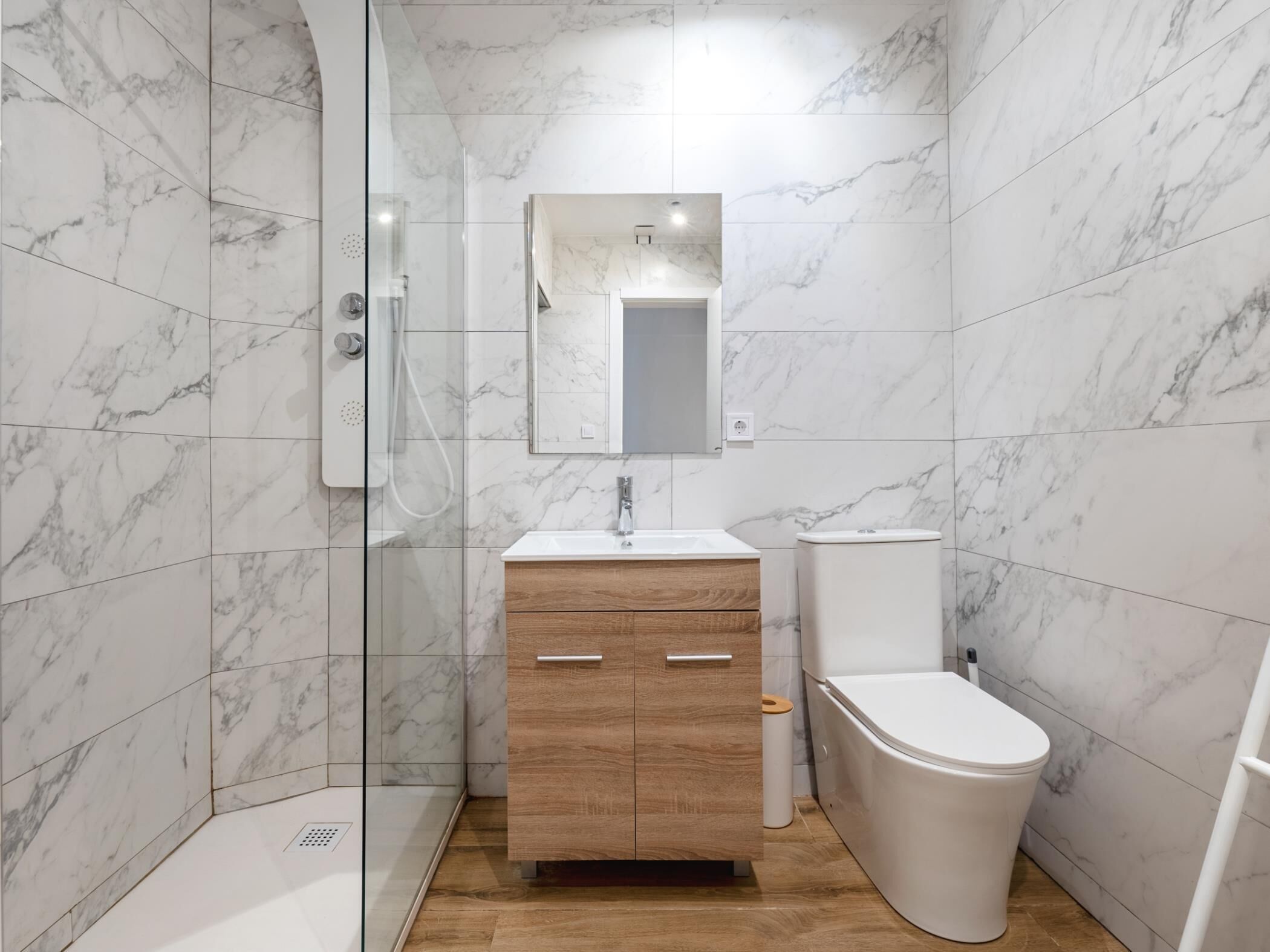 A modern bathroom with a glass shower enclosure, a wooden vanity with a mirror, and a white toilet.