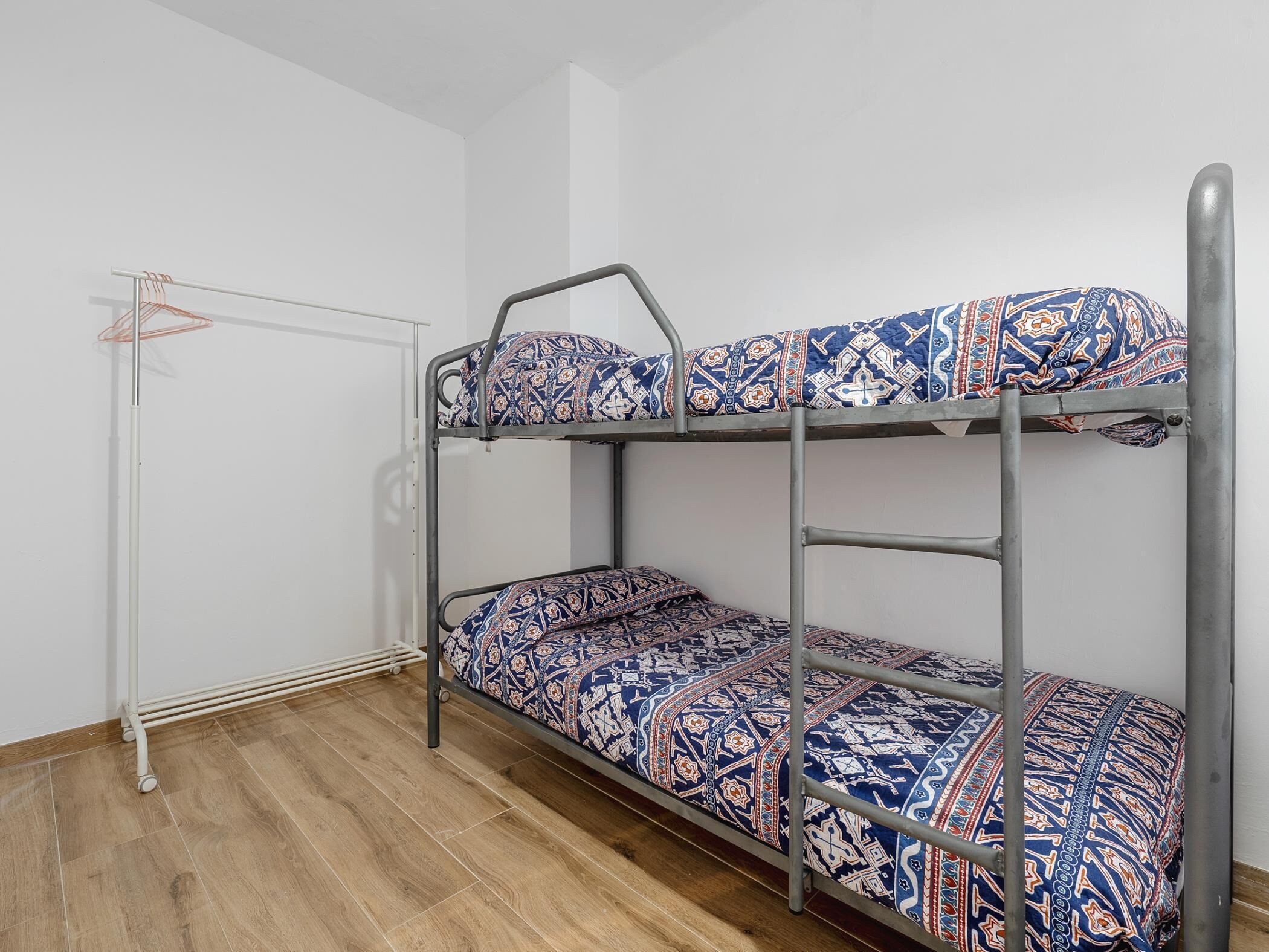 A bunk bed with patterned bedding in a room with wooden flooring and a white wall.