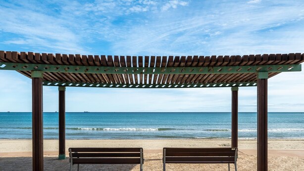 A beach with a wooden pergola and two benches.