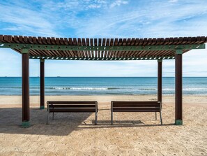 Una playa con una pérgola de madera y dos bancos.