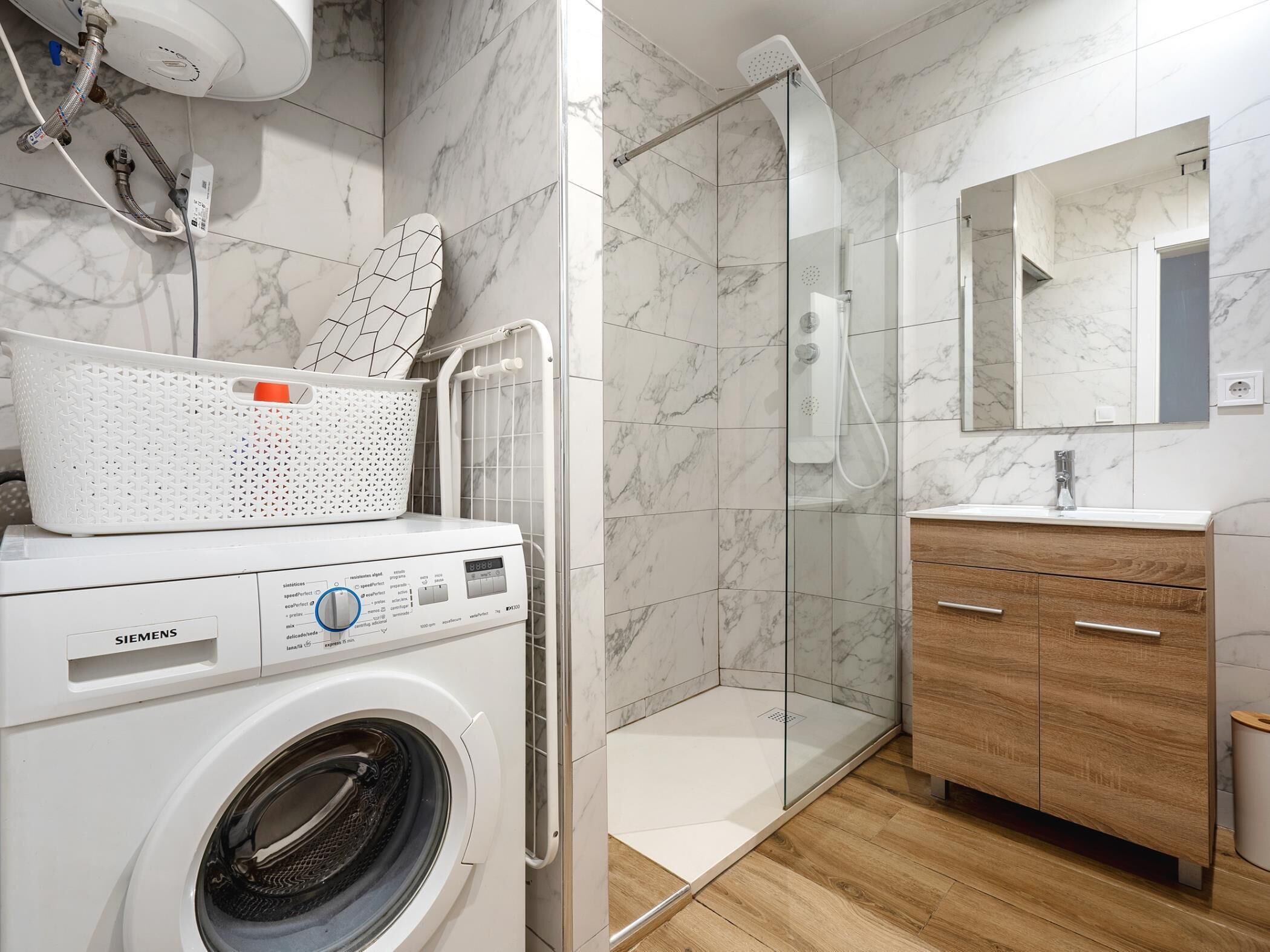 Une salle de bain moderne équipée d’un lave-linge, d’une douche à parois de verre et d’un meuble-lavabo en bois.