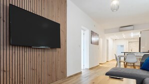A modern living room with a flat-screen TV mounted on a wooden wall, a wooden coffee table, and a grey sofa.