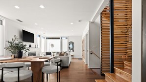 A modern kitchen with a dining area, wooden staircase, and a flat-screen TV. - Luxury 3 Bed/3 Bath NEW Home in Ruston (Tacoma)