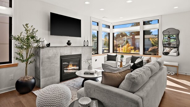 A modern living room with a fireplace, a flat-screen TV, and large windows offering a view of the outdoors. - Luxury 3 Bed/3 Bath NEW Home in Ruston (Tacoma)