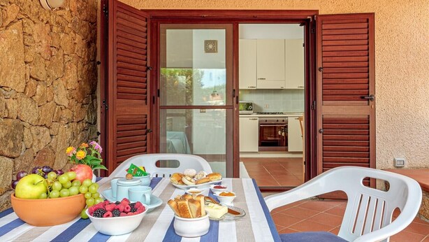 Une table de petit-déjeuner avec des fruits, des viennoiseries, et une vue sur la cuisine à travers une porte vitrée.