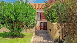 Un chemin menant à une maison avec un toit en tuiles, entourée d’une végétation luxuriante et d’un portail en bois.