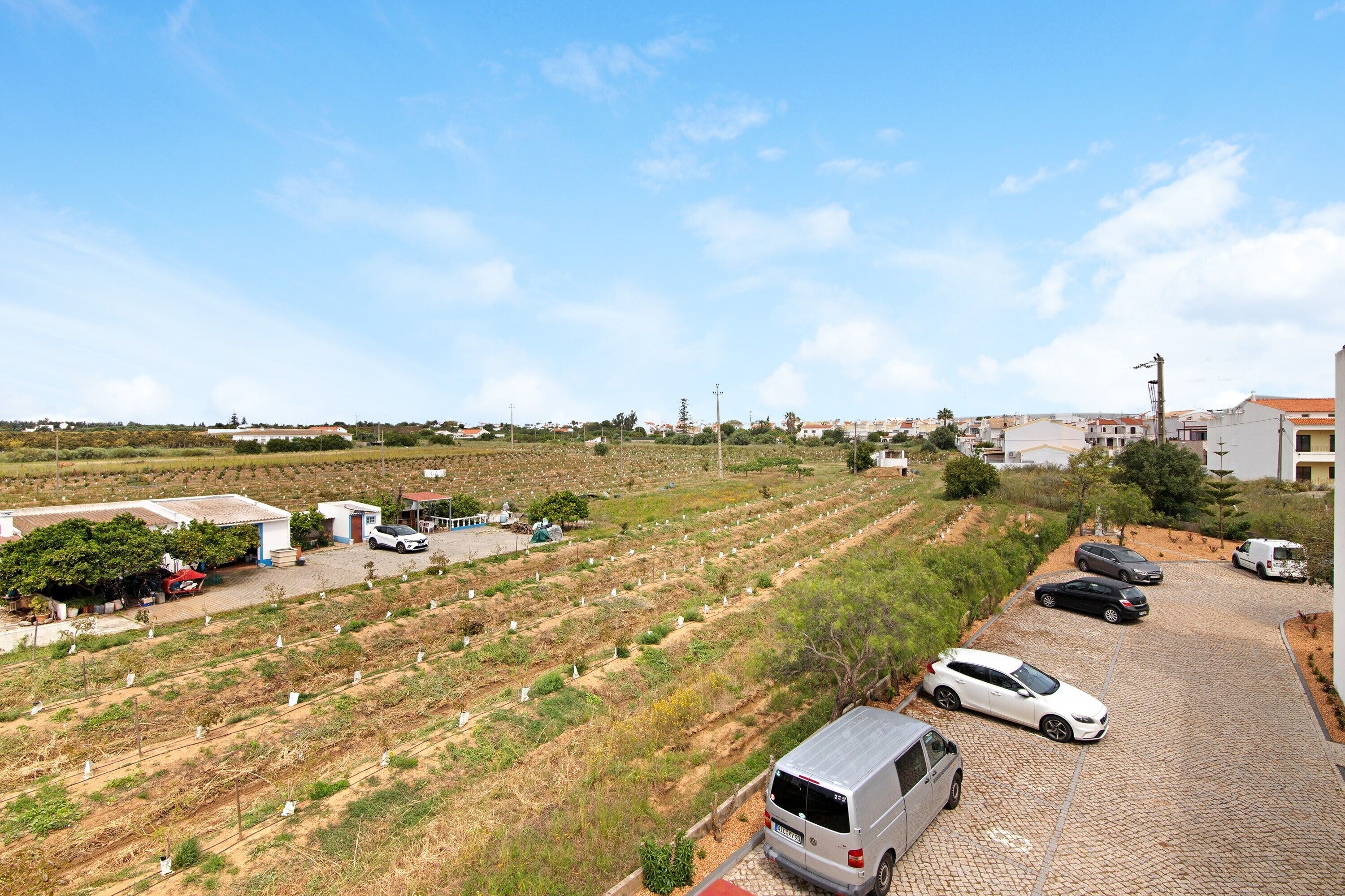 Una zona residencial con aparcamiento pavimentado, una hilera de casas y un campo con lápidas.