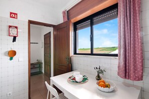 Una cocina con una mesa de comedor, dos tazas, un plato con fruta y una ventana que da al campo.