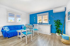 Une pièce avec un canapé bleu, des chaises blanches, une petite table, un meuble et une plante en pot.