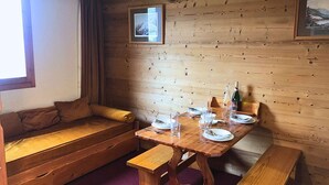 Una habitació acollidora amb zona d'seureure a partir d'una cadira de fusta, taula de menjador de fusta preparada per a dues persones i finestra amb cortines.