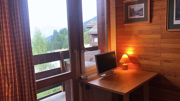 Una habitación con estructura de madera, una mesa de trabajo, una computadora portátil y una lámpara encendida.