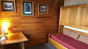 Una habitación de madera con una cama, un escritorio con una lámpara y tres cuadros en la pared.