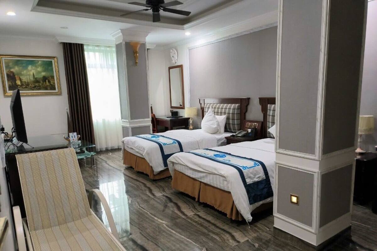 Quarto de hotel com duas camas, área de estar com uma poltrona, escrivaninha e um espelho grande.