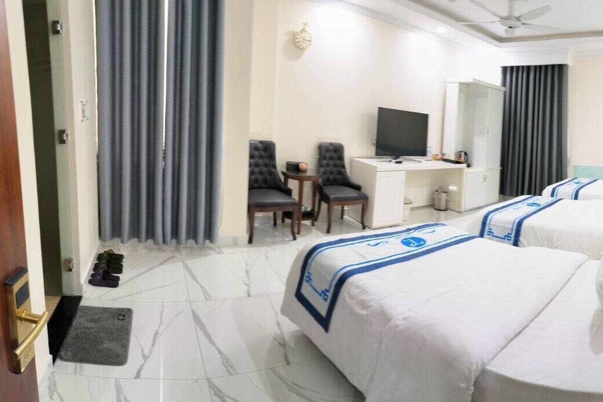 Quarto de hotel com duas camas, uma escrivaninha, uma cadeira, uma televisão e um guarda-roupa.