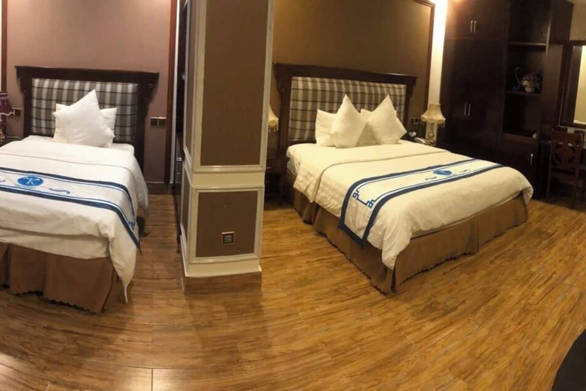 Quarto de hotel com duas camas, soalho em madeira, uma secretária com cadeira e um guarda-roupa.