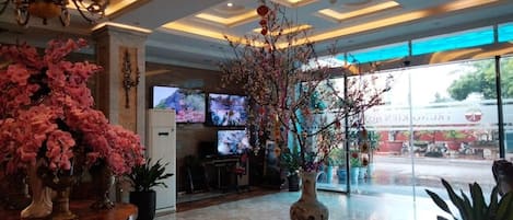 Un vestíbulo con un gran jarrón de flores rosadas, una araña y una pantalla de televisión.