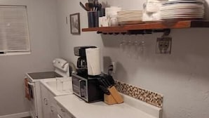 Una cocina compacta con gabinetes blancos, un microondas, una cafetera y un cesto de basura.