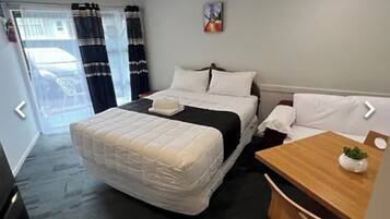 A hotel room with a bed, a wooden desk, a chair, and a small table with a plant.